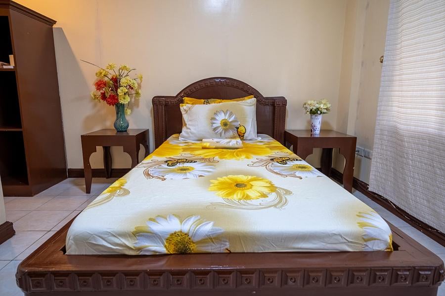 Single bed with yellow floral bedding in a quiet guest room at Pecan Pension House, Iloilo
